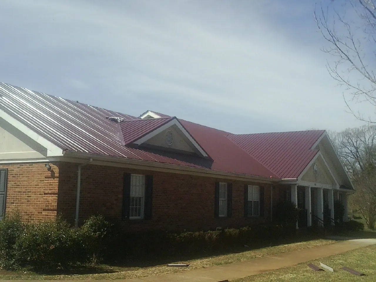 Red metal roof with gabled entries on a long brick building, from a Hail Damage Roof Repair job in Burnsville