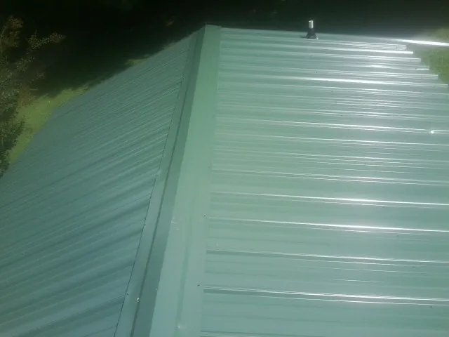 New green metal panels meeting at the ridge of a roof — Flat Roof Repair work by our crew in Burnsville