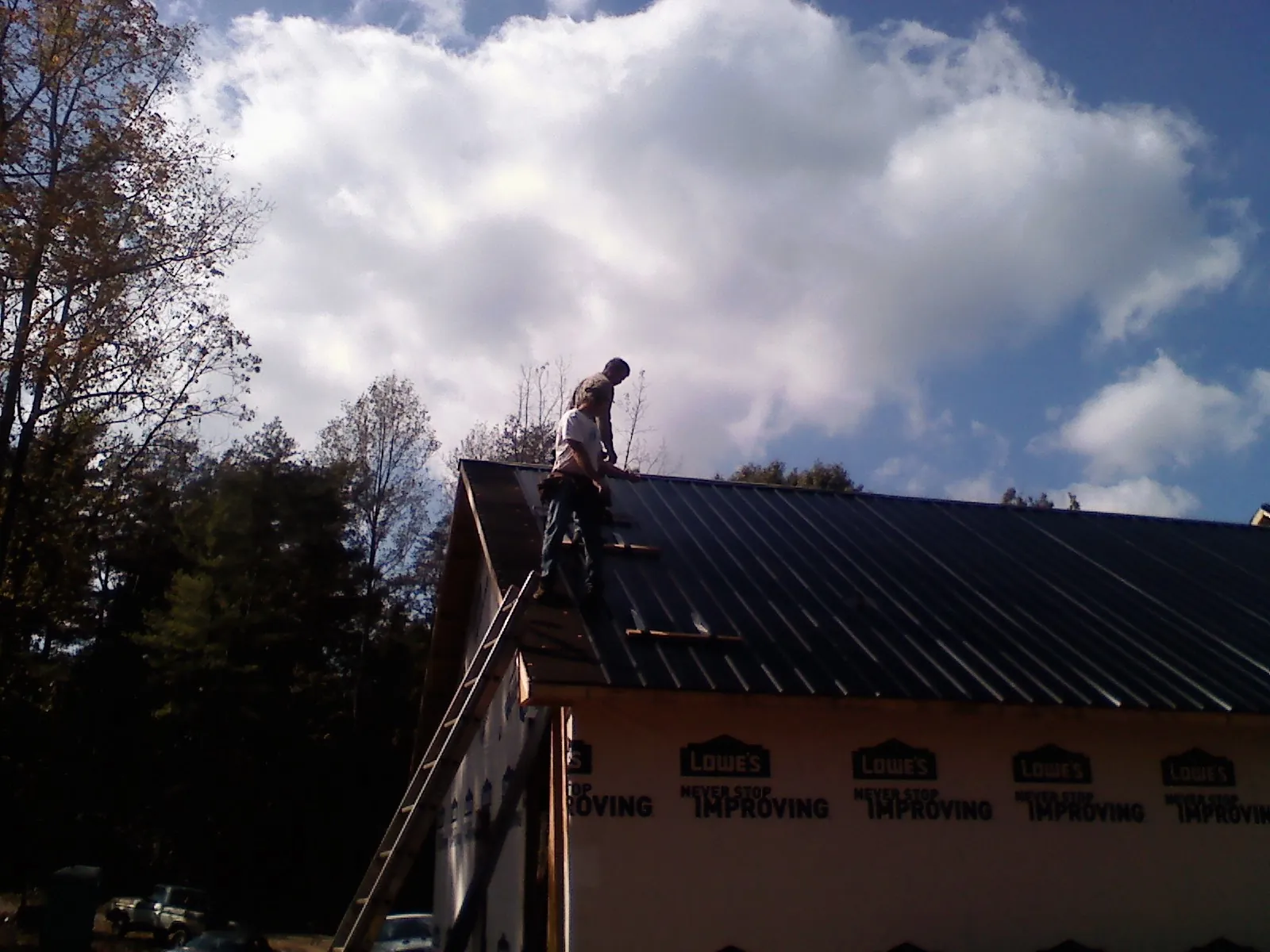 Roofer fastening dark metal panels high against a cloudy sky, from a Roof Inspection job in Burnsville